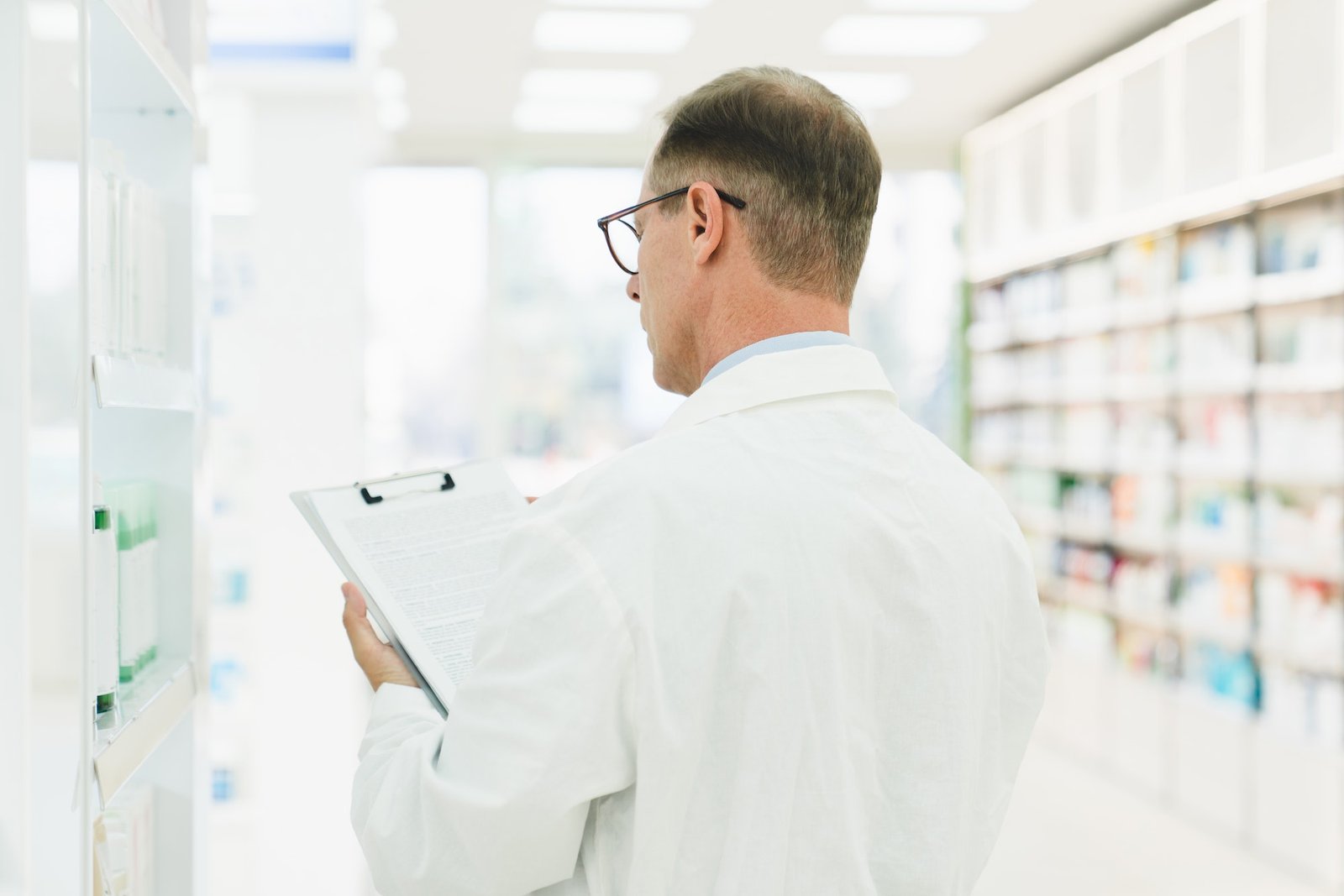Chemist checking medical prescription on clipboard, looking for medicines, vitamins at pharmacy